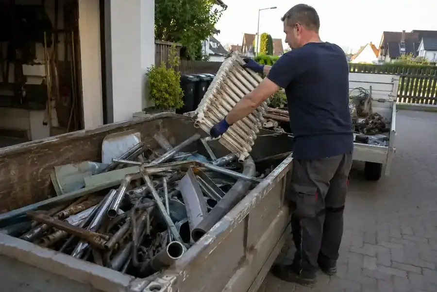 Handwerker entleert Gerüst- und Metallreste in Container – Baustellenentsorgung für Handwerksbetriebe