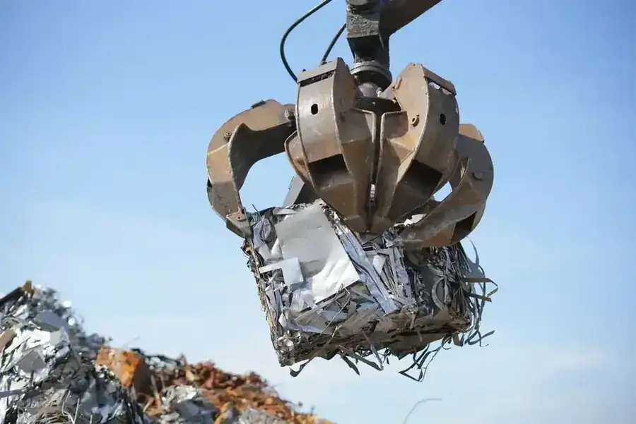 Schrotthändler mit Greifer – hydraulischer Polypgreifer lädt gepressten Metallschrott auf einem Recyclinghof in NRW